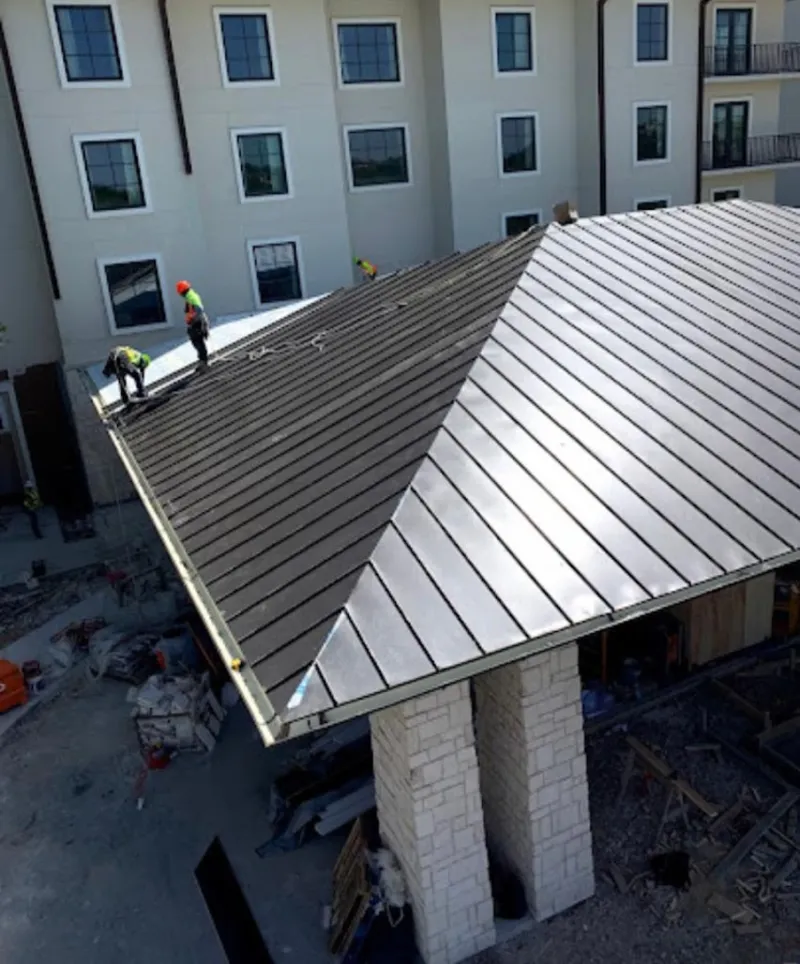 Crew installing standing seam metal roof panels on a commercial project in Summerfield